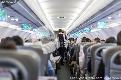 Image of Interior of commercial airplane with stewardess serving passengers on seats during flight.