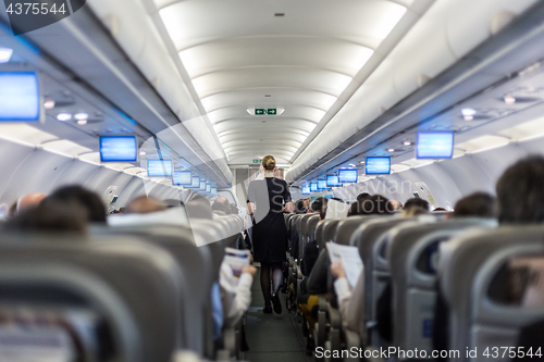 Image of Interior of commercial airplane with stewardess serving passengers on seats during flight.