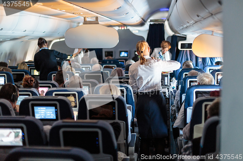 Image of Interior of large commercial airplane with stewardesses serving passengers on seats during flight.