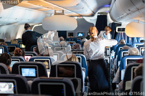 Image of Interior of large commercial airplane with stewardesses serving passengers on seats during flight.