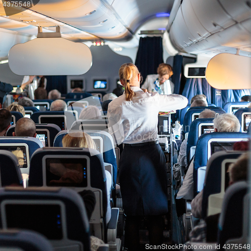 Image of Interior of large commercial airplane with stewardesses serving passengers on seats during flight.