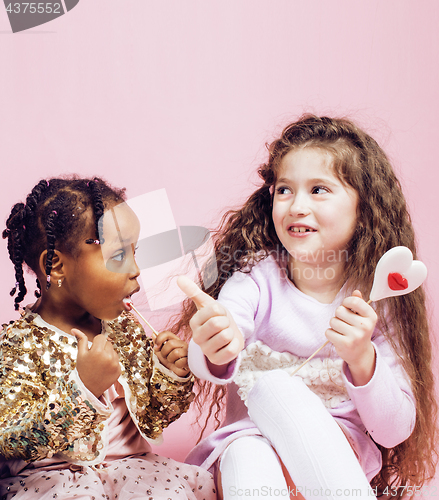 Image of lifestyle people concept: diverse nation children playing together, caucasian girl with african little girl holding candy happy smiling close up on pink background