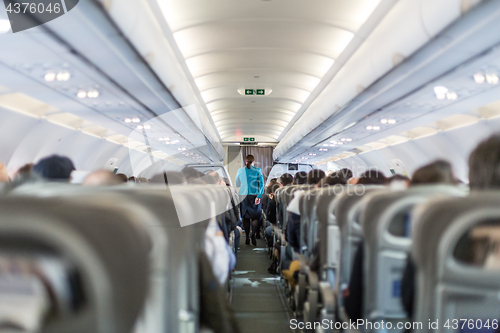 Image of Interior of commercial airplane with stewardess serving passengers on seats during flight.