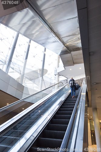 Image of Businesswoman with large black bag and mobile phone ascending on escalator.