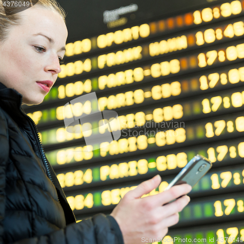 Image of Woman at airport in front of flight information board checking her phone.