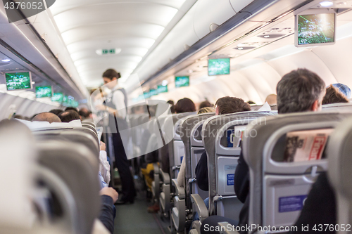 Image of Interior of commercial airplane with stewardess serving passengers on seats during flight.