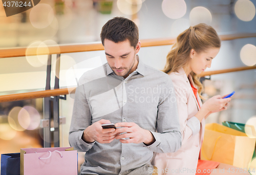 Image of couple with smartphones and shopping bags in mall