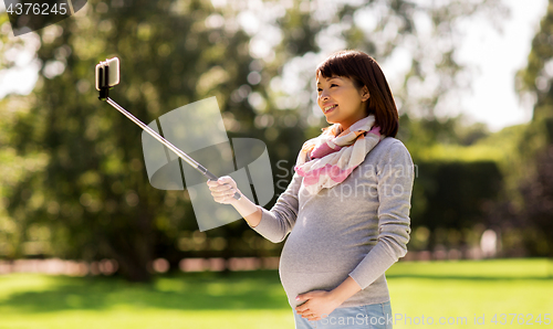 Image of happy pregnant asian woman taking selfie at park