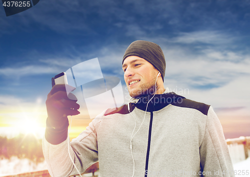 Image of happy man with earphones and smartphone in winter