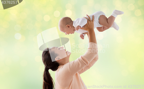 Image of happy mother playing with little baby over green