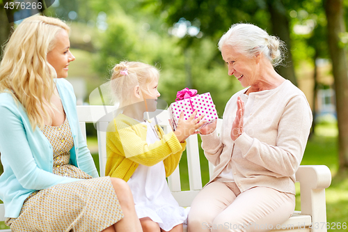 Image of happy family giving present to grandmother at park