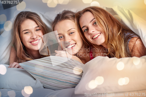 Image of happy young women in bed at home pajama party