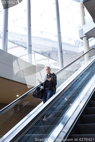 Image of Businesswoman with large black bag and mobile phone descending on escalator.