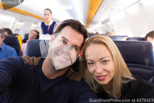 Image of Young handsome couple taking a selfie on commercial airplane.