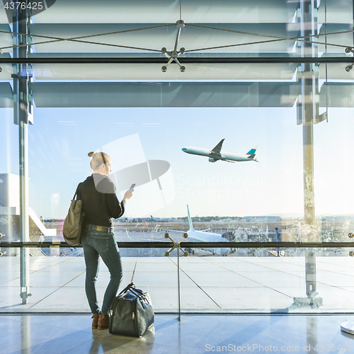 Image of Young woman waiting at airport, looking through the gate window.