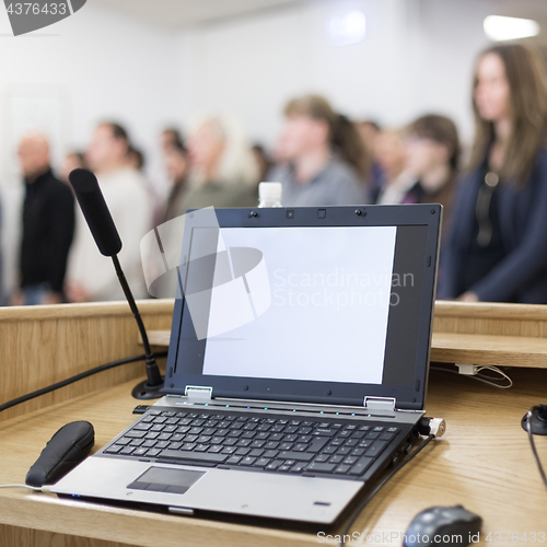 Image of Laptop and microphone on the rostrum in lecture hall full of conference participants.