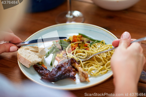 Image of hands of woman eating pasta and roast chicken