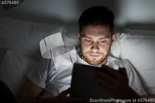 Image of young man with tablet pc in bed at home bedroom