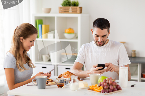 Image of couple with smartphones having breakfast at home