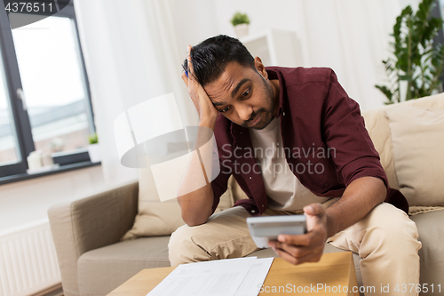 Image of confused man with papers and calculator at home