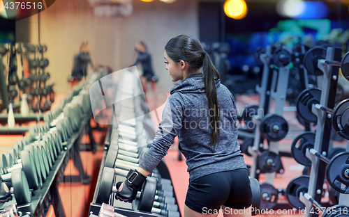 Image of young woman choosing dumbbells in gym