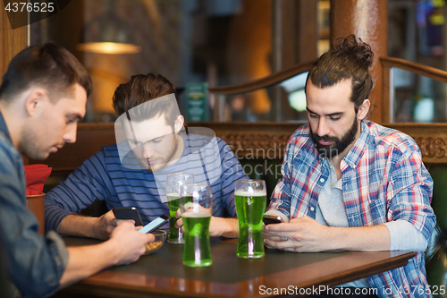 Image of friends with smartphones and green beer at pub