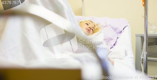 Image of Bedridden female patient recovering after surgery in hospital care.