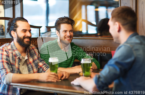 Image of male friends drinking green beer at bar or pub