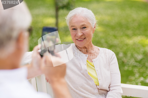 Image of old woman photographing man by smartphone in park