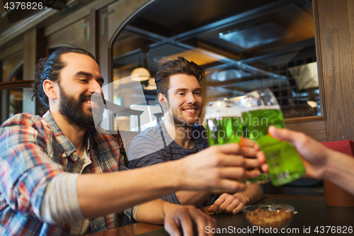 Image of male friends drinking green beer at bar or pub