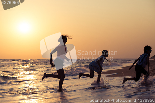 Image of Happy children playing on the beach at the sunset time.