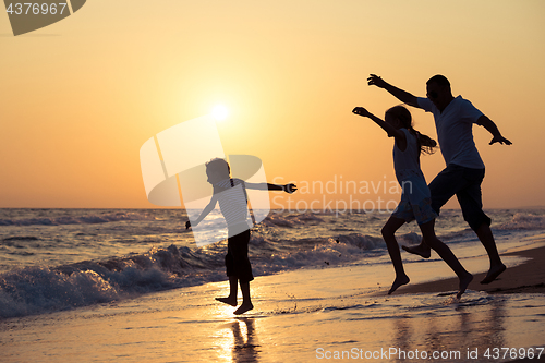 Image of Father son and daughter playing on the beach at the sunset time.