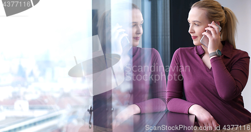 Image of Elegant Woman Using Mobile Phone by window in office building