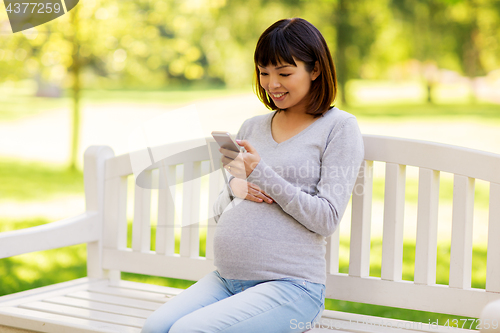 Image of happy pregnant asian woman with smartphone at park