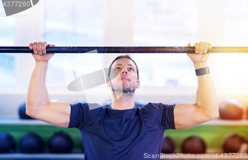 Image of man exercising on bar and doing pull-ups in gym