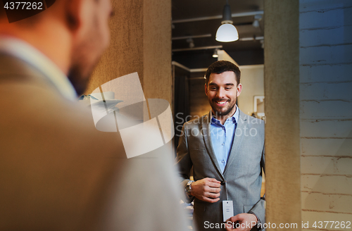 Image of man trying jacket on at mirror in clothing store