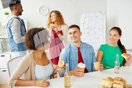 Image of happy friends or team eating at office