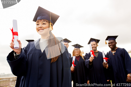 Image of happy students in mortar boards with diplomas