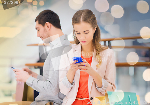 Image of couple with smartphones and shopping bags in mall