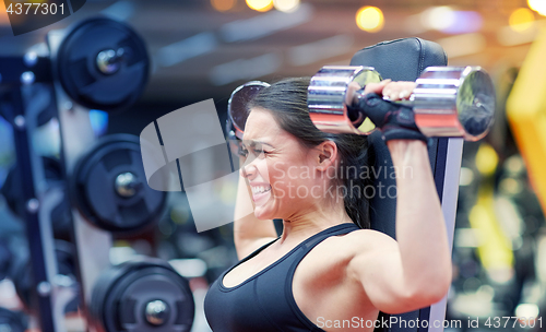 Image of young woman flexing muscles with dumbbell in gym