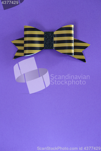 Image of Black and golden striped bow tie over ultra violet background.