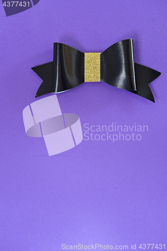 Image of Black and golden bow tie over ultra violet background.