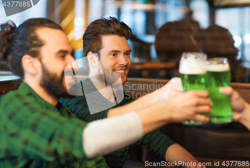 Image of male friends drinking green beer at bar or pub