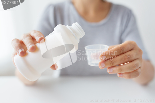 Image of woman pouring syrup from bottle to medicine cup