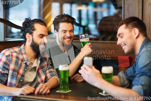 Image of friends with smartphone drinking green beer at pub