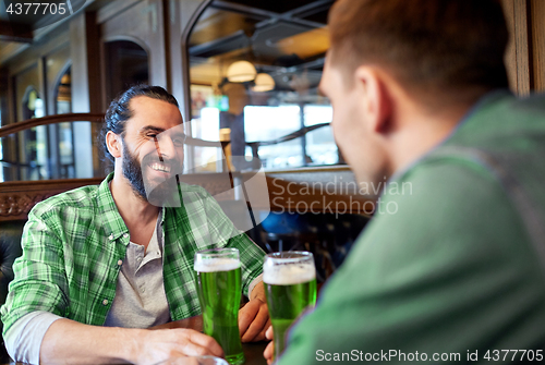 Image of male friends drinking green beer at bar or pub