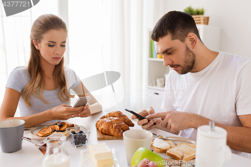 Image of couple with smartphones having breakfast at home