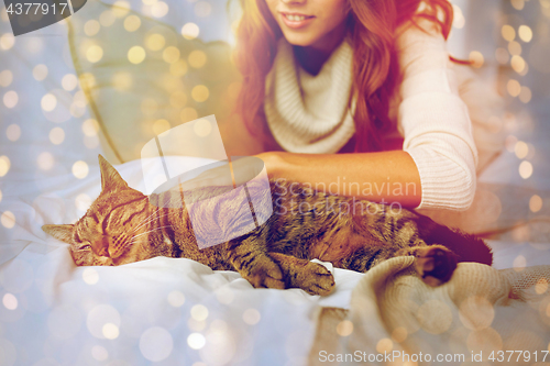 Image of happy young woman with cat lying in bed at home