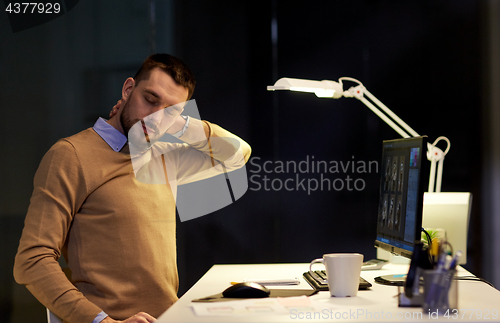 Image of tired man having neck ache working at night office