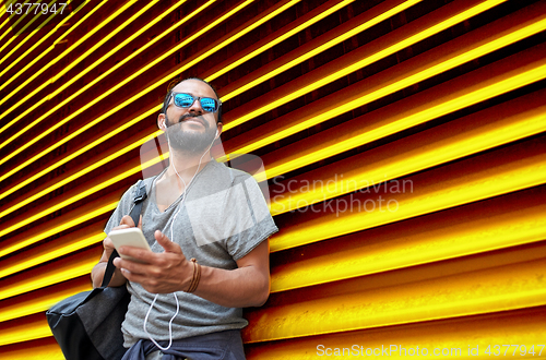 Image of man with earphones and smartphone over wall